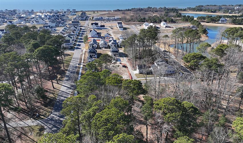 Aerial view of Bay Creek showing completed roads, newly built coastal homes, wooded areas, and the Chesapeake Bay in the background, illustrating early 2026 residential construction progress at this rural EB5 community.