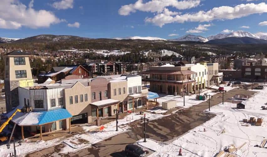 Drone view of Market Street buildings at Grand Park with exterior facades taking shape, sidewalks and streets visible, and surrounding mountain landscape highlighting progress within the rural EB5 development during winter conditions.