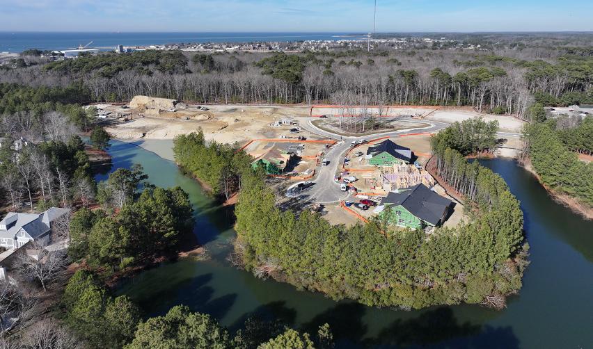 Elevated drone view of Bay Creek construction near winding waterways, showing framed homes, cleared lots, and ongoing infrastructure installation within the rural EB5 master-planned community.
