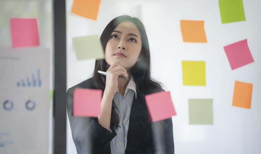 A professional woman reviewing notes on a glass board, representing EB5 investors evaluating rural versus urban projects, weighing visa benefits, processing timelines, and risk factors