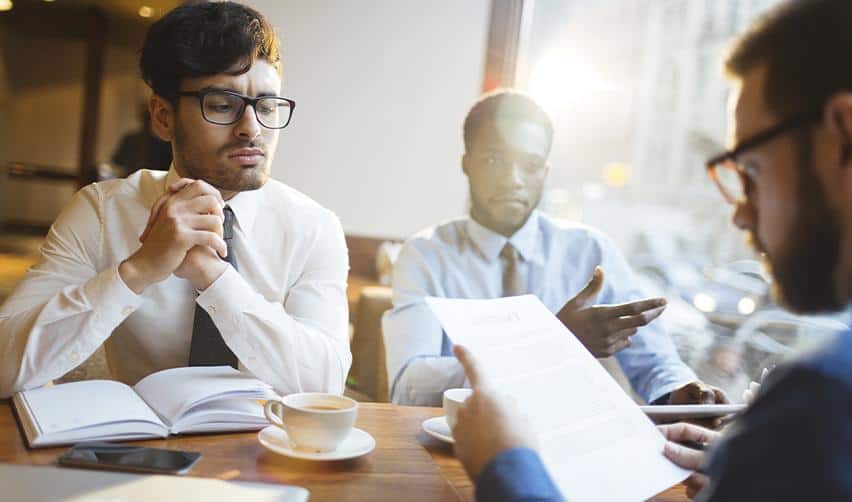 Three professionals discussing documents at a meeting table, symbolizing EB5 investors conducting due diligence and comparing regional center track records before making an investment decision.