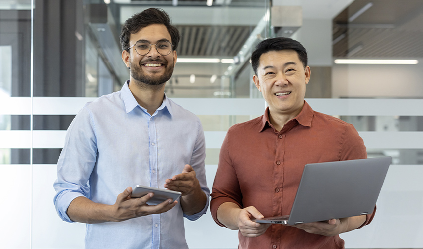Two business professionals holding a tablet and laptop in a modern office, representing Chinese and Indian EB5 investors comparing visa timelines and project options in 2026.