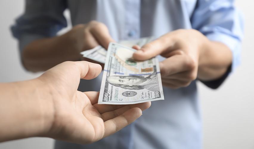 A close-up of one person handing U.S. dollar bills to another, illustrating the return of investment capital and repayment considerations in the EB5 process.