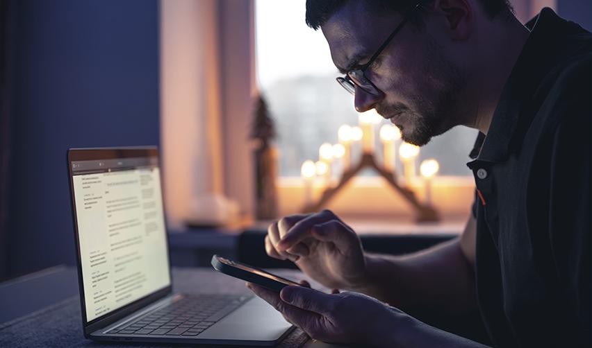Man using a smartphone beside a laptop at home, representing an EB5 investor or family member using ChatGPT to explore U.S. job options, entrepreneurship, and career planning.