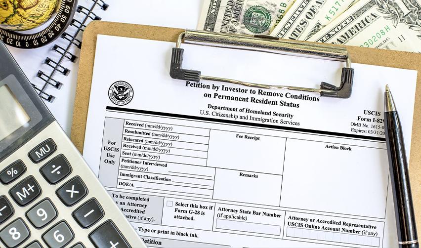 A Form I-829 petition on a clipboard with U.S. currency, a calculator, and a pen, symbolizing the final stage of the EB5 process and the relationship between immigration milestones and return of capital.